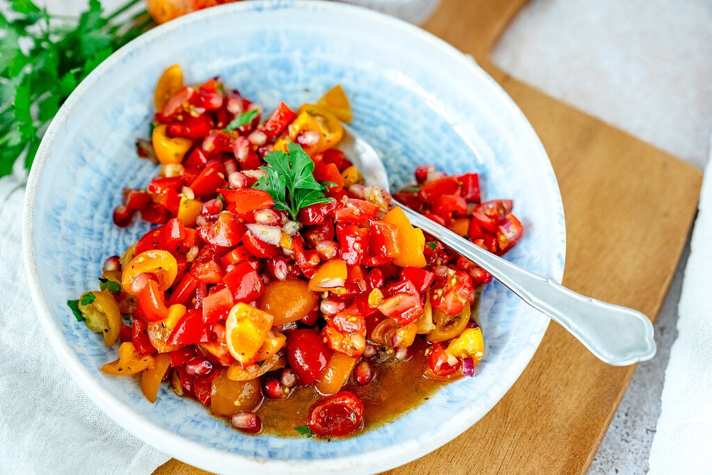 Leckerer Tomaten-Granatapfel-Salat im Querformat, in einem blauen Teller angerichtet.