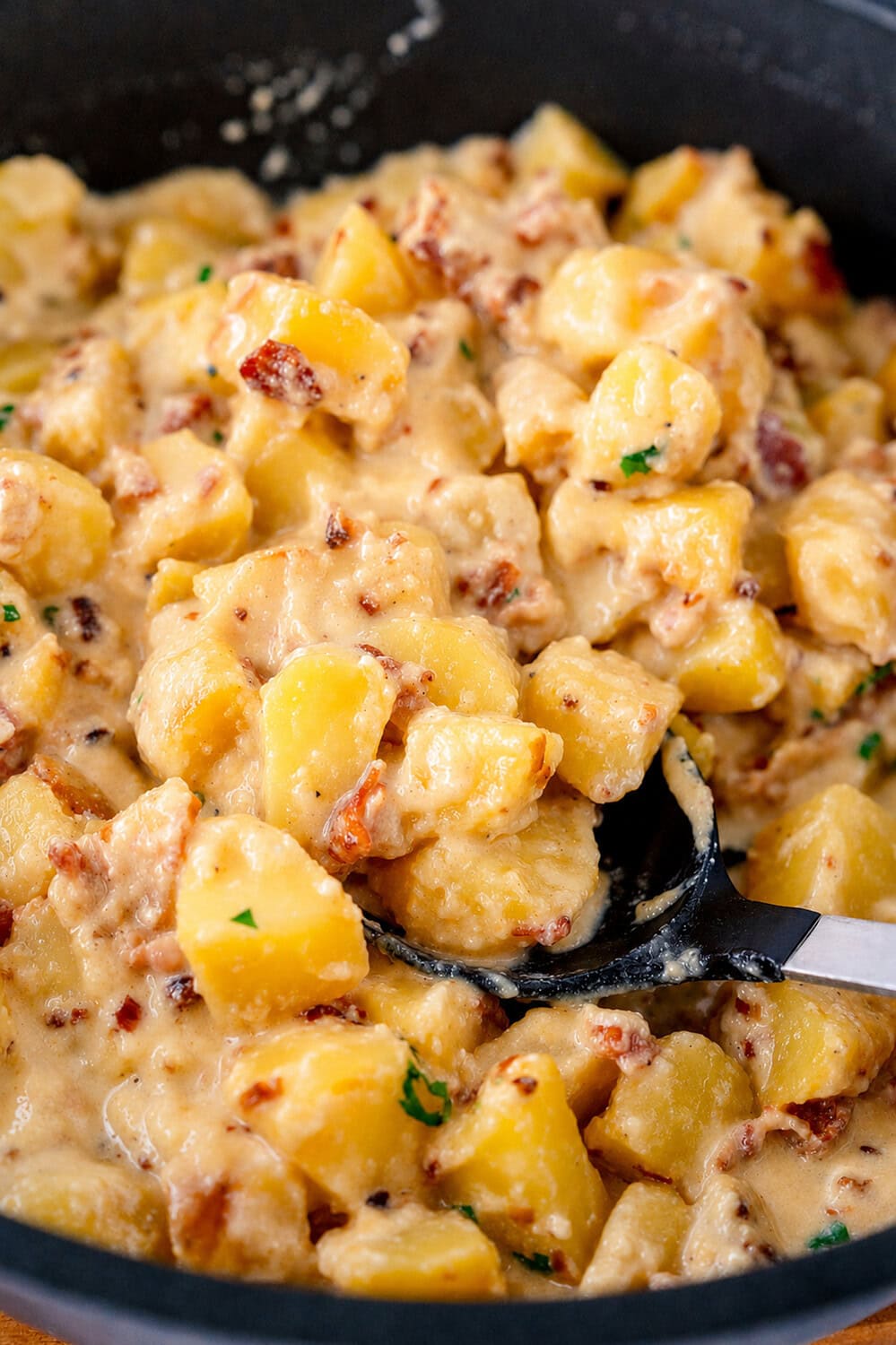 Kartoffel-Carbona-Pfanne in der Nahaufnahme Ein Löffel holt Kartoffeln hoch, die von einer cremigen Sauce umgeben sind