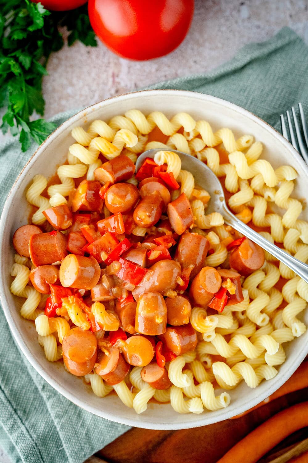 Topview auf eine Bowl mit Spiralnudeln mit kleingeschnittenen Würstchen mit Paprika, Sauce und einem Löffel darin