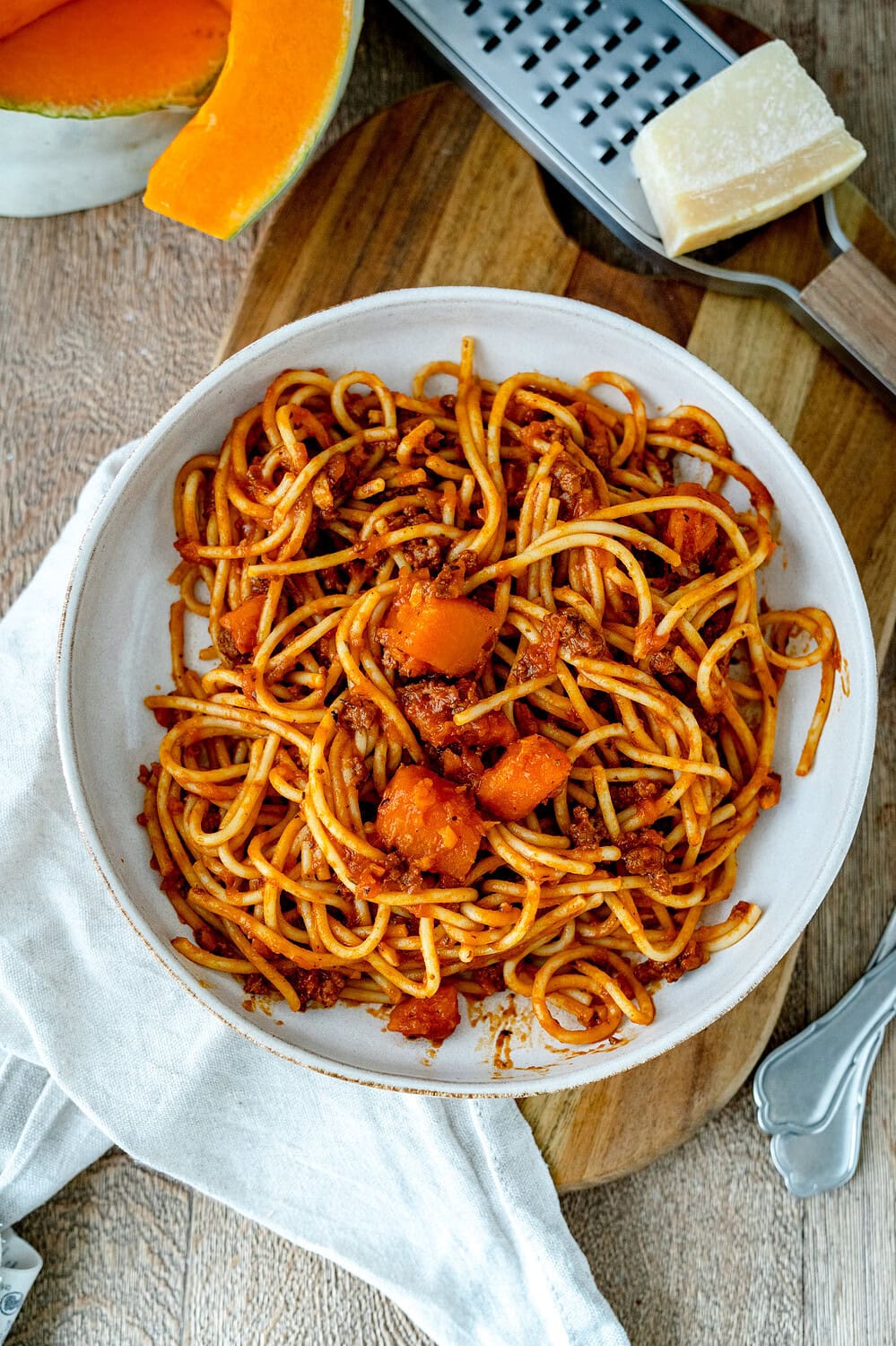 Kürbis Bolognese TOpview auf einem Holzbrett, Kürbis im Hintergrund und eine Reibe mit Parmesan