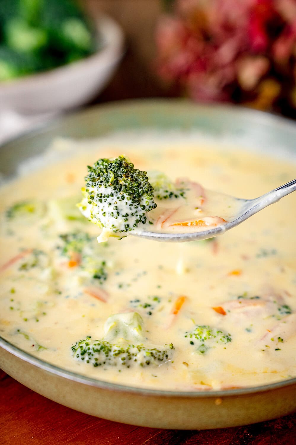 Löffel mit Brokkoli-Cheddar-Suppe mit einem Brokkoliröschen und Möhren darauf.