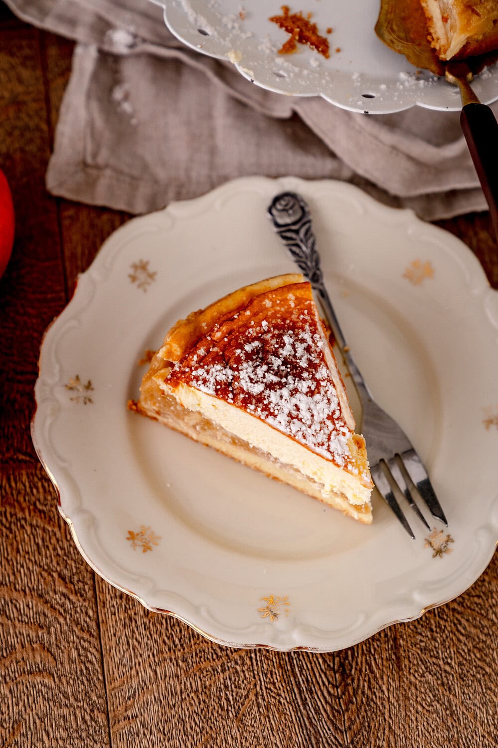 Topview auf ein Stück Apfelmus-Schmandkuchen auf geblümten Teller mit Gabel daneben