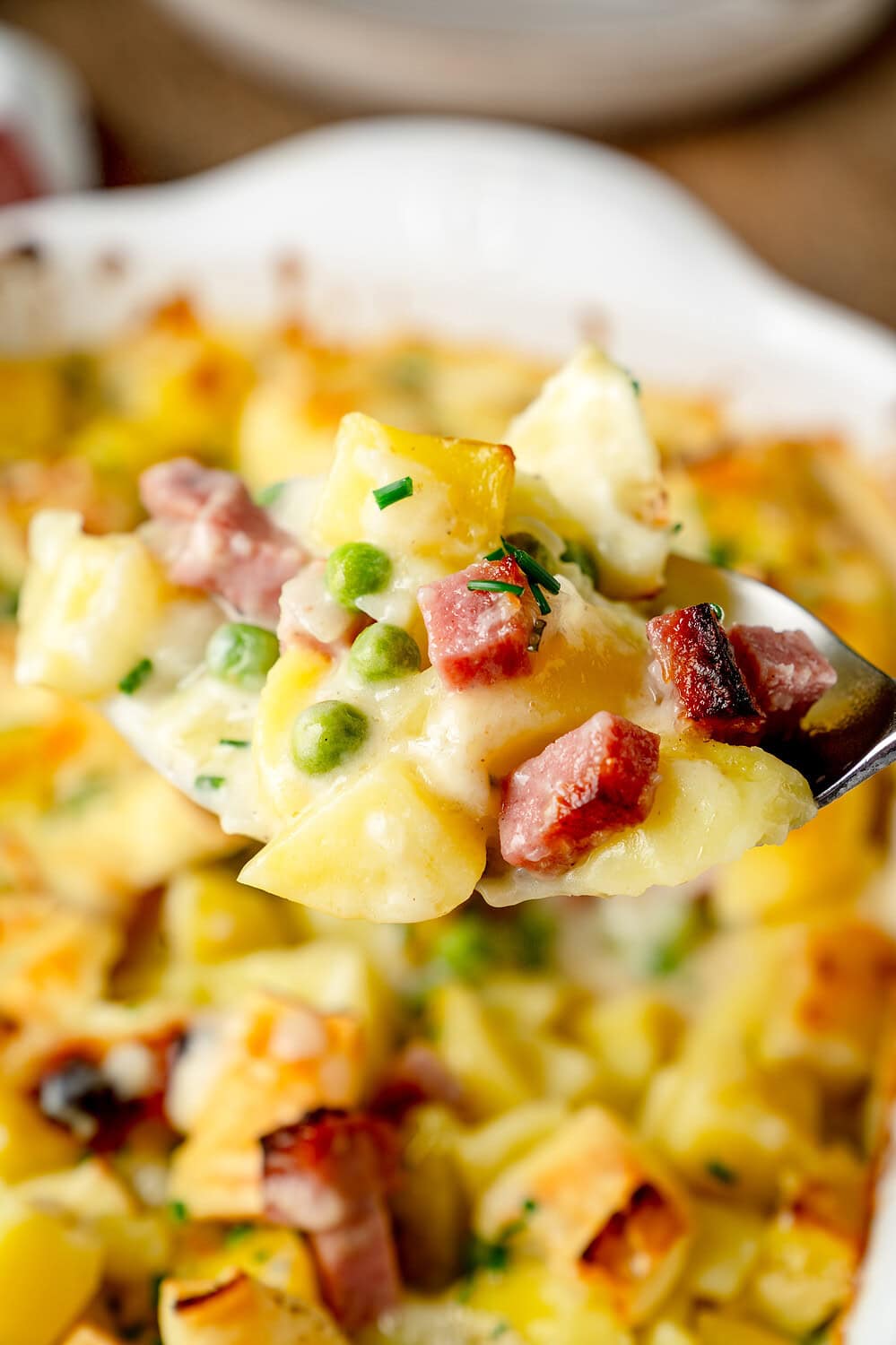 Ein Löffel voll Kartoffelauflauf mit Salami und Erbsen in der Nahaufnahme